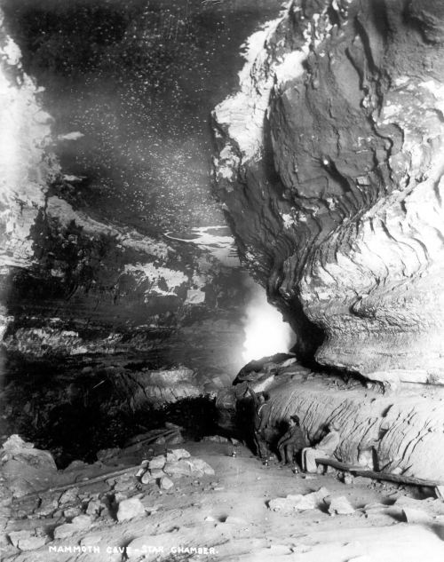 A black and white photo of Mammoth Cave's Star Chamber, showcasing large rock formations and a dimly lit cavern.