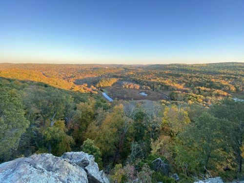 A panoramic view of a colorful autumn landscape with rolling hills and a winding river under a clear blue sky.