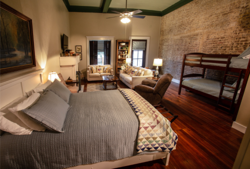 Cozy bedroom with a queen bed, bunk beds, seating area, and exposed brick walls, featuring warm wooden floors.