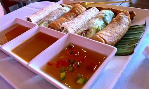 A platter of assorted spring rolls served with two dipping sauces, garnished with herbs and vegetables.