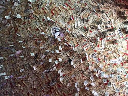 A wall covered in various dollar bills and notes, featuring handwritten messages and signatures.