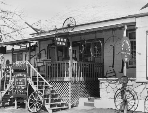 Black and white image of a rustic country dining establishment with wooden steps and vintage decor.