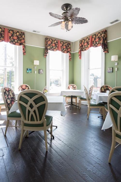 A bright dining room with green walls, floral curtains, and elegant tables set for guests.