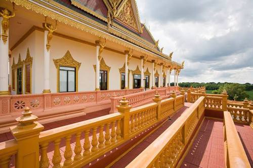 A beautifully designed temple exterior with ornate golden details and a pink balcony, set against a cloudy sky.