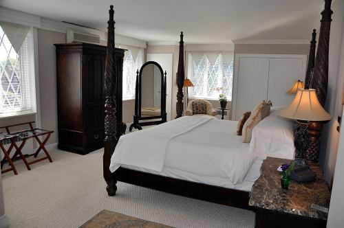 A spacious bedroom featuring a four-poster bed, elegant furniture, and large windows with natural light.