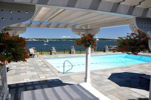 A serene poolside view with hanging flowers, overlooking a calm lake and distant boats under a clear blue sky.