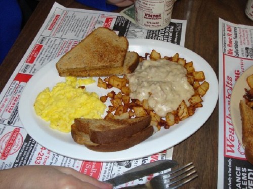 A plate of breakfast featuring scrambled eggs, diced potatoes with gravy, toast, and slices of dark bread.