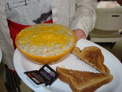 A person holds a plate with a bowl of cheesy soup and two slices of toasted bread on the side.