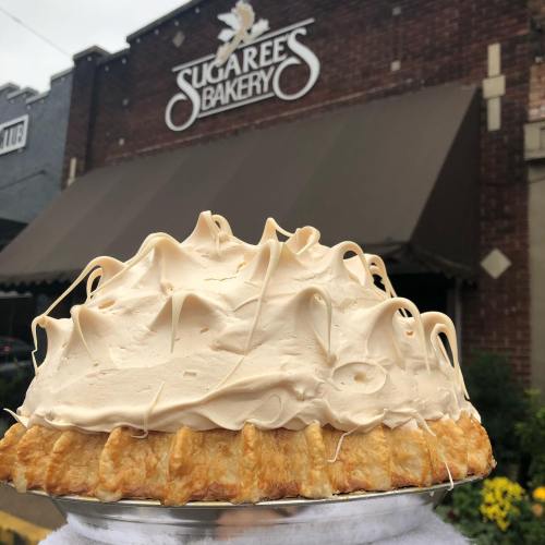 A delicious pie with a creamy topping, displayed in front of Sugaree's Bakery, featuring a brick facade and awning.