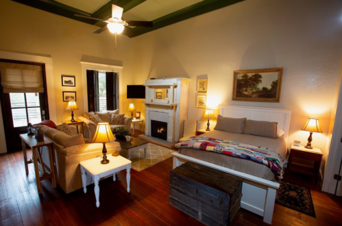 Cozy bedroom with a bed, sofa, fireplace, and warm lighting, featuring rustic decor and wooden floors.