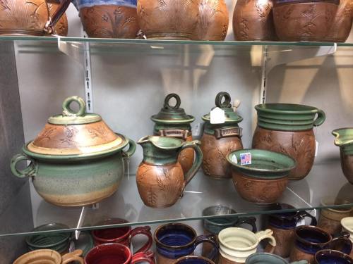 A display of various handcrafted pottery pieces, including bowls, pitchers, and a lidded pot, in earthy tones.