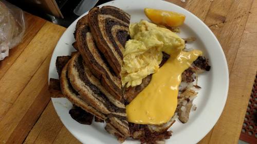 A plate with marbled toast, scrambled eggs, melted cheese, and hash browns, garnished with a slice of orange.