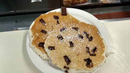 Two large pancakes with chocolate chunks, dusted with powdered sugar, served on a white plate.