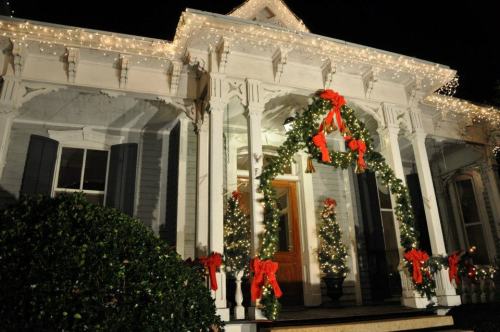 A beautifully decorated house for Christmas, featuring lights, garlands, and red bows on the porch and windows.