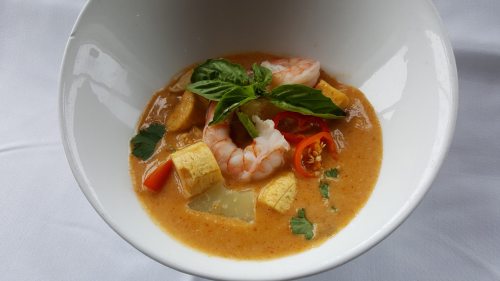 A bowl of shrimp soup with coconut milk, vegetables, and herbs, garnished with basil and chili slices.