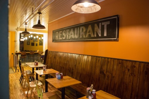 Cozy restaurant interior with wooden tables, chairs, and a large "RESTAURANT" sign on the orange wall.