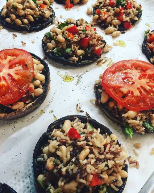 Stuffed portobello mushrooms topped with tomatoes, rice, and vegetables on a baking sheet.