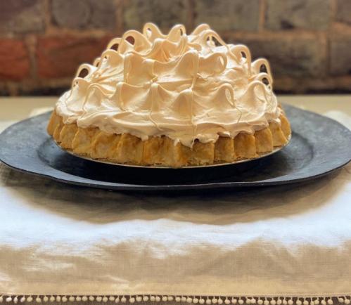 A beautifully baked pie with a golden crust and fluffy meringue topping, displayed on a black plate.