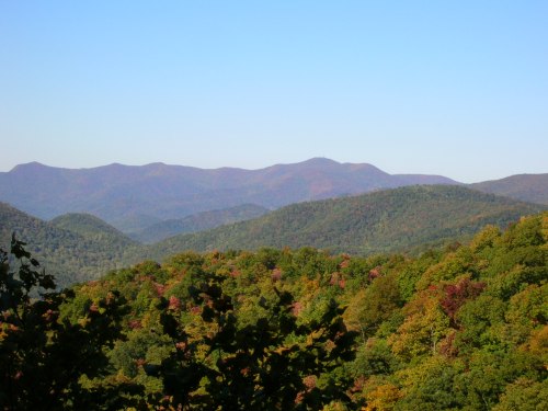 A scenic view of rolling mountains covered in autumn foliage under a clear blue sky.
