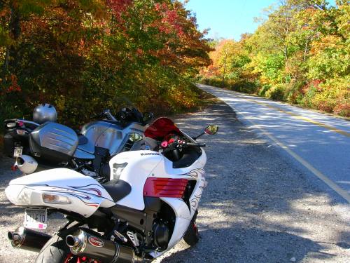 Two motorcycles parked beside a scenic road lined with vibrant autumn foliage.
