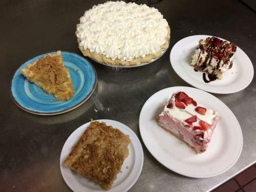 A variety of desserts on plates: a pie topped with whipped cream, layered cakes, and crumbly treats.