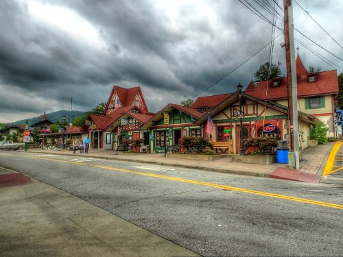 Charming alpine-style buildings line a street under a cloudy sky, with shops and colorful signs inviting visitors.