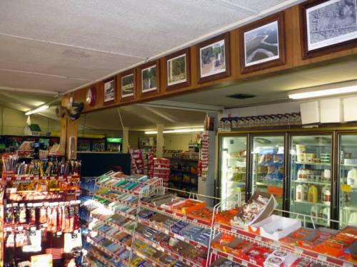 Interior of a convenience store featuring shelves of snacks, drinks, and framed photos on the wall.
