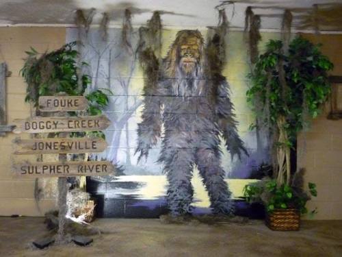 A mural of a Bigfoot figure surrounded by foliage and wooden signs pointing to nearby locations.