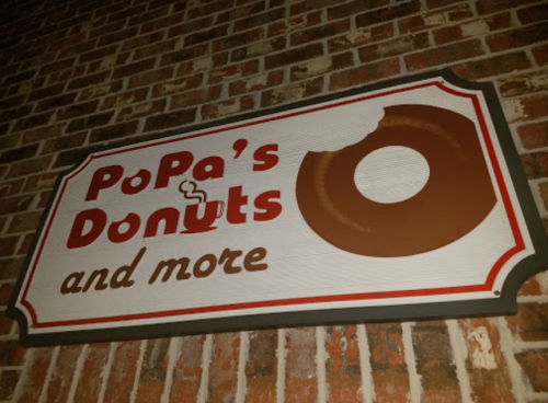 Sign for PoPa's Donuts featuring a donut graphic and the text "Donuts and more" against a brick background.