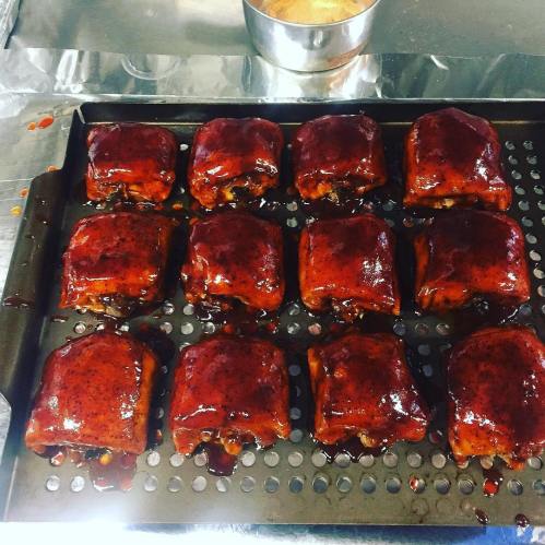 A tray of barbecue-glazed meat squares, arranged in a grid, with a small bowl of sauce in the background.