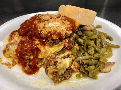 A plate of lasagna topped with marinara sauce, cheese, and a side of green beans and bread.