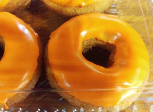 Two orange-glazed donuts in a clear plastic container.