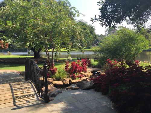 A serene garden scene with a wooden bridge, colorful flowers, and a calm lake in the background under a clear blue sky.