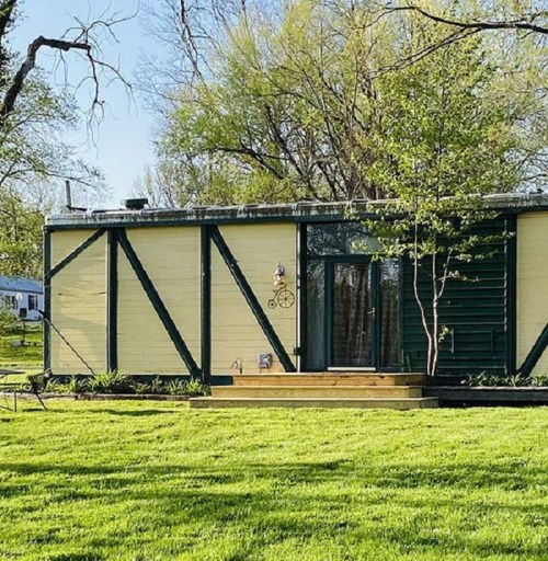 A modern, single-story house with a yellow and green exterior, surrounded by lush green grass and trees.