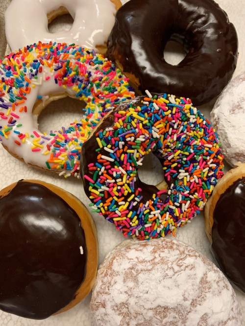 A variety of donuts, including chocolate, glazed, and sprinkled, arranged on a light background.