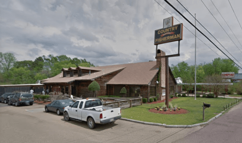 A rustic log cabin-style restaurant with a sign reading "Country Fisherman," surrounded by trees and parked cars.
