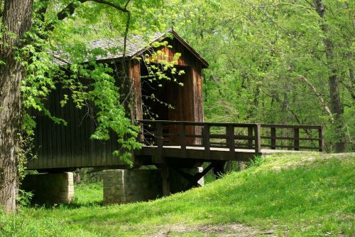 A rustic wooden covered bridge surrounded by lush green trees and grass.