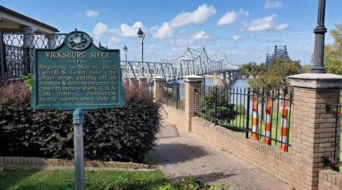 Sign marking the Vicksburg Siege, with a view of a bridge and river under a clear blue sky.