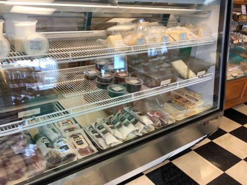 A display case filled with various cheeses, meats, and condiments in a deli setting.