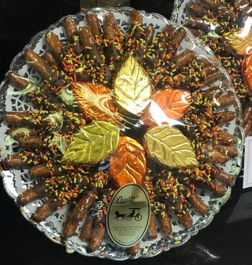A decorative platter of chocolate-covered pretzels with colorful sprinkles and autumn-themed leaves.