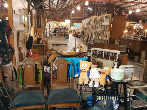 A vintage shop interior filled with furniture, toys, and various collectibles, including chairs and stuffed animals.
