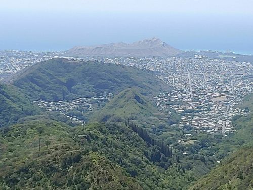 A panoramic view of lush green mountains overlooking a coastal city and ocean in the distance.