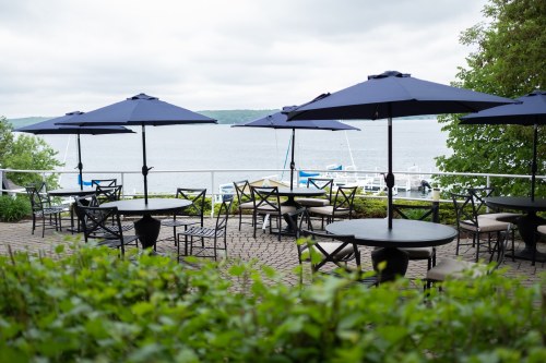 Outdoor dining area with black tables and navy umbrellas overlooking a calm lake and greenery.