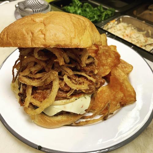 A hearty burger topped with crispy fried onions, cheese, and served with potato chips on a white plate.