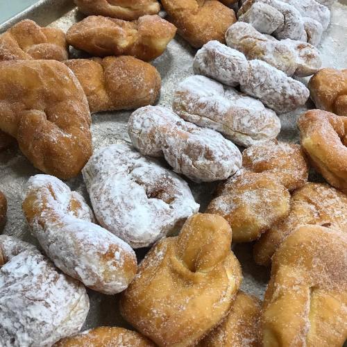 A tray of assorted fried pastries, some coated in powdered sugar, showcasing various shapes and textures.