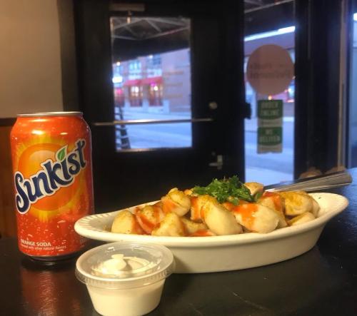 A bowl of dumplings topped with sauce and parsley, next to a can of Sunkist orange soda, with a door in the background.