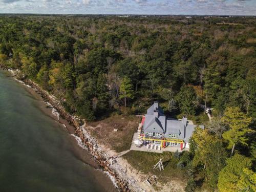 Aerial view of a colorful house by the water, surrounded by trees and rocky shoreline under a partly cloudy sky.