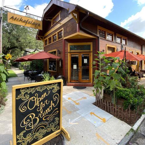 A cozy restaurant exterior with outdoor seating, featuring a sign that says "Open for Brunch." Trees in the background.