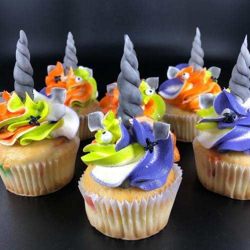 Colorful unicorn-themed cupcakes with vibrant frosting and gray horn decorations, set against a black background.
