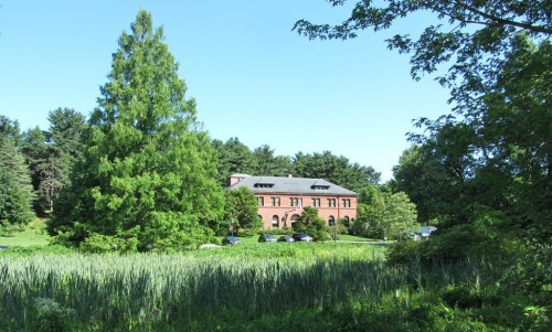 A brick building surrounded by greenery and trees, set against a clear blue sky.